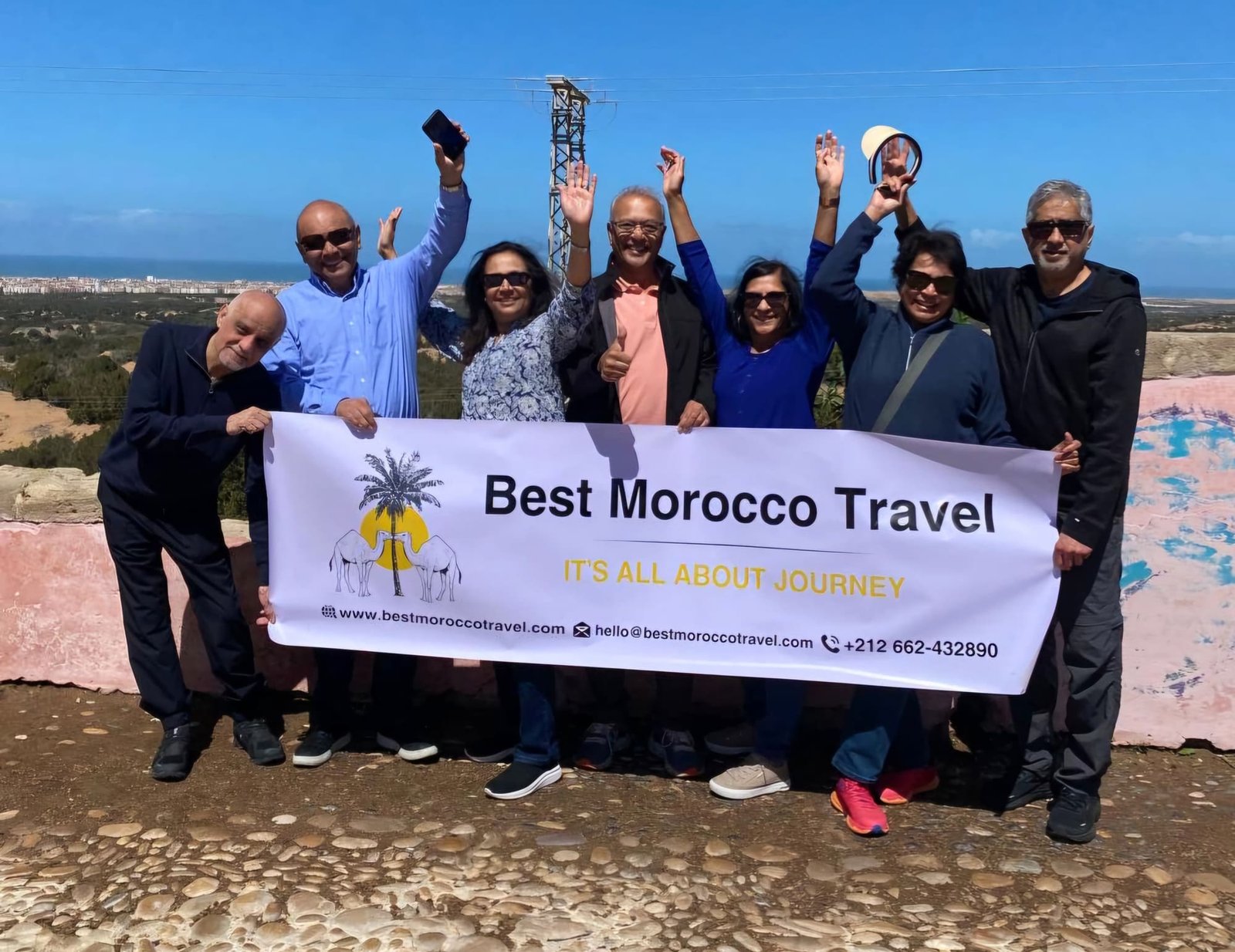 A group of our guests with the Best Morocco Travel banner on a mountain viewpoint